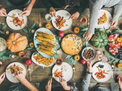 Vegan or vegetarian Thanksgiving, Friendsgiving holiday celebration. Flat-lay of friends eating at Thanksgiving Day table with pumpkin pie, roasted vegetables, fruit and rose wine, top view